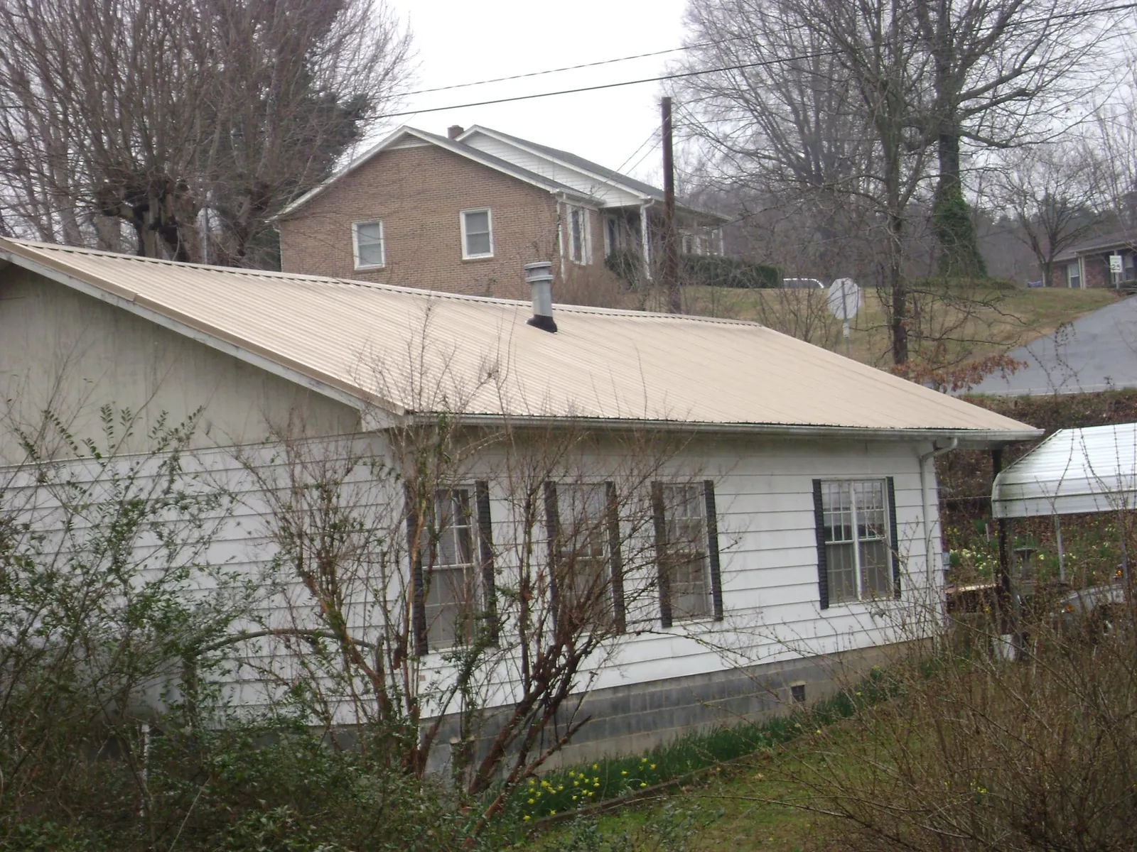 Tan metal roof on a white sided house set into a hillside — Commercial Roofing by Roofing Brothers in Piedmont